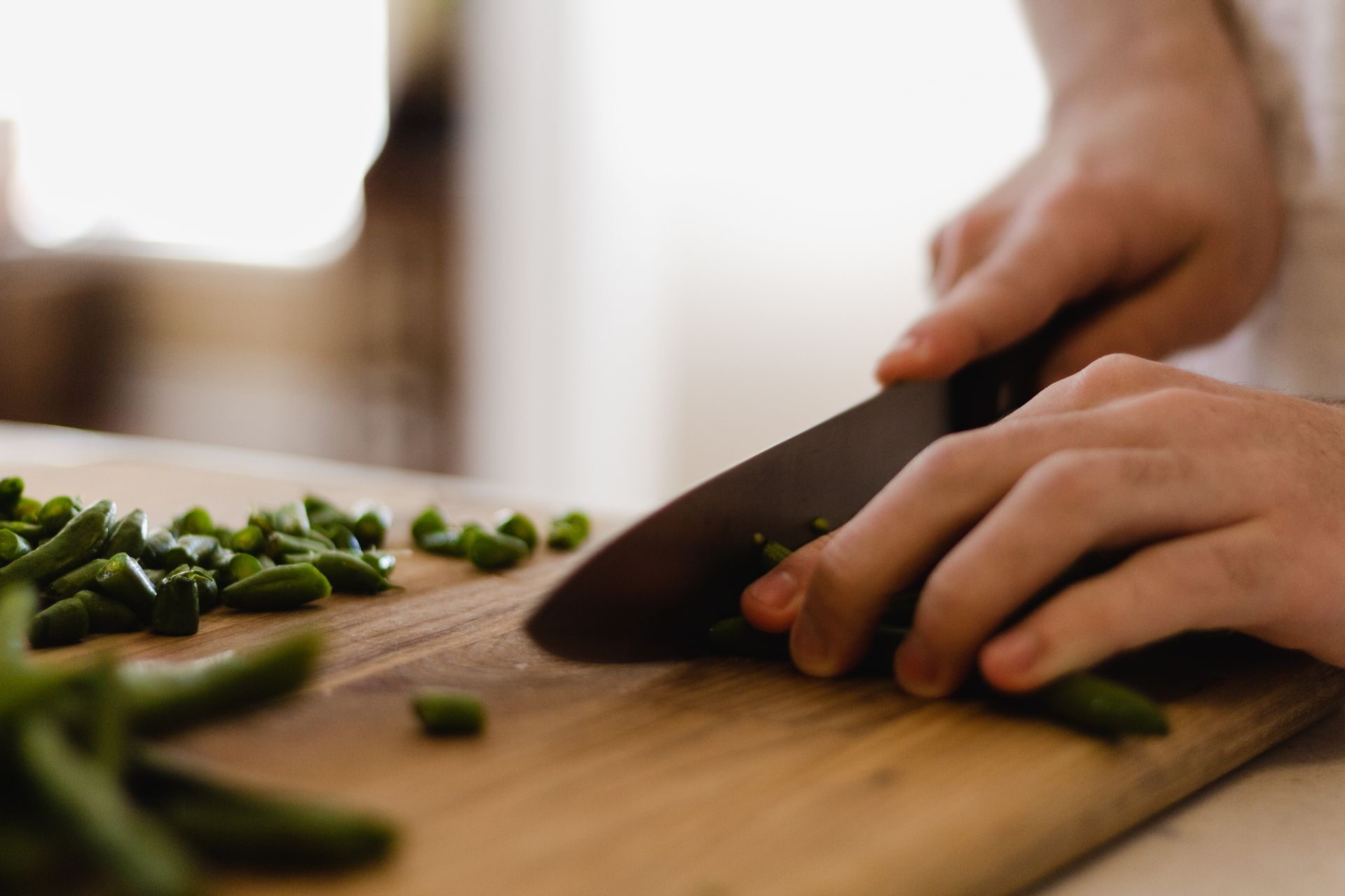 Personne coupant des haricots verts frais au couteau sur une planche à découper