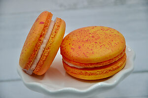 Deux macarons à la mangue vanille/citron posés sur une assiette, garnis d’une crème fruitée jaune et légèrement brillante.